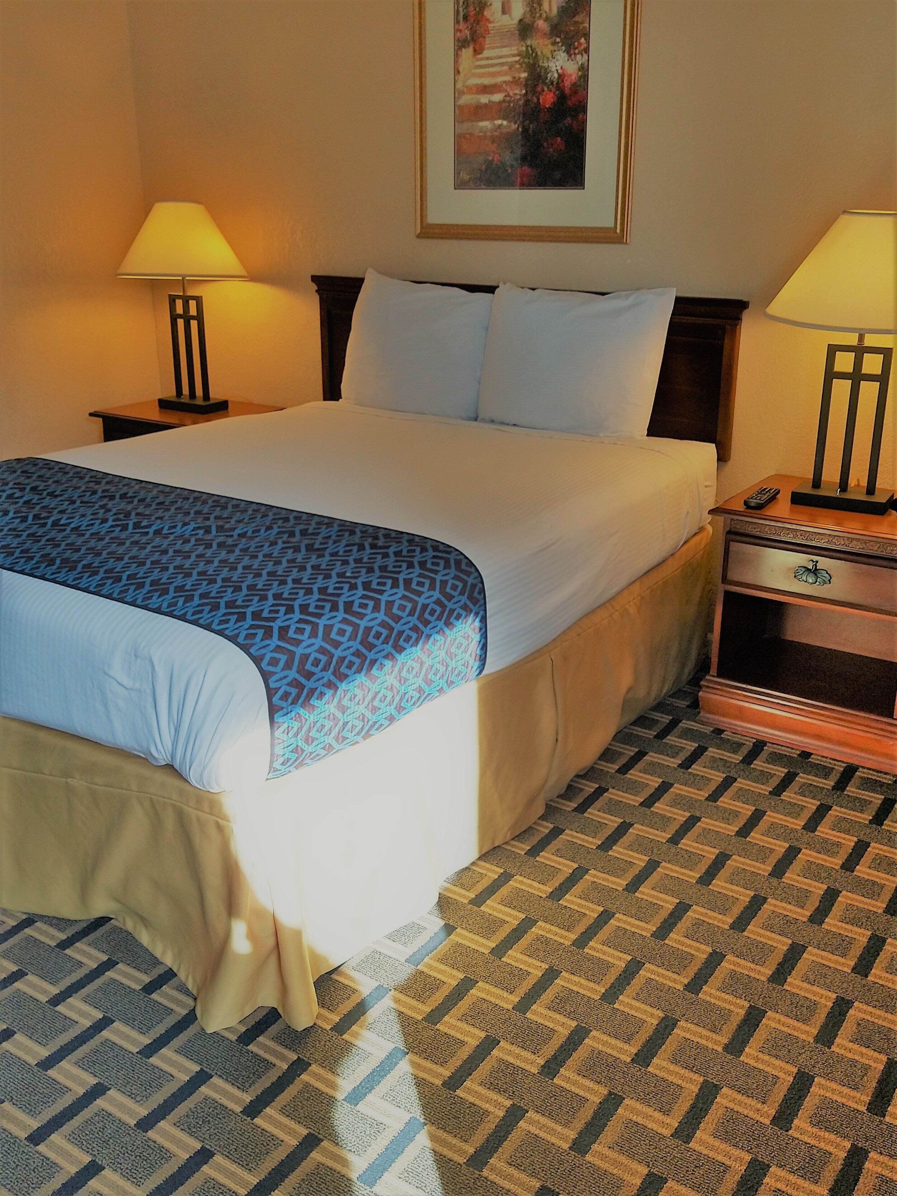 A neatly made bed with a patterned bedspread, two bedside tables with lamps, and a framed picture on the wall.