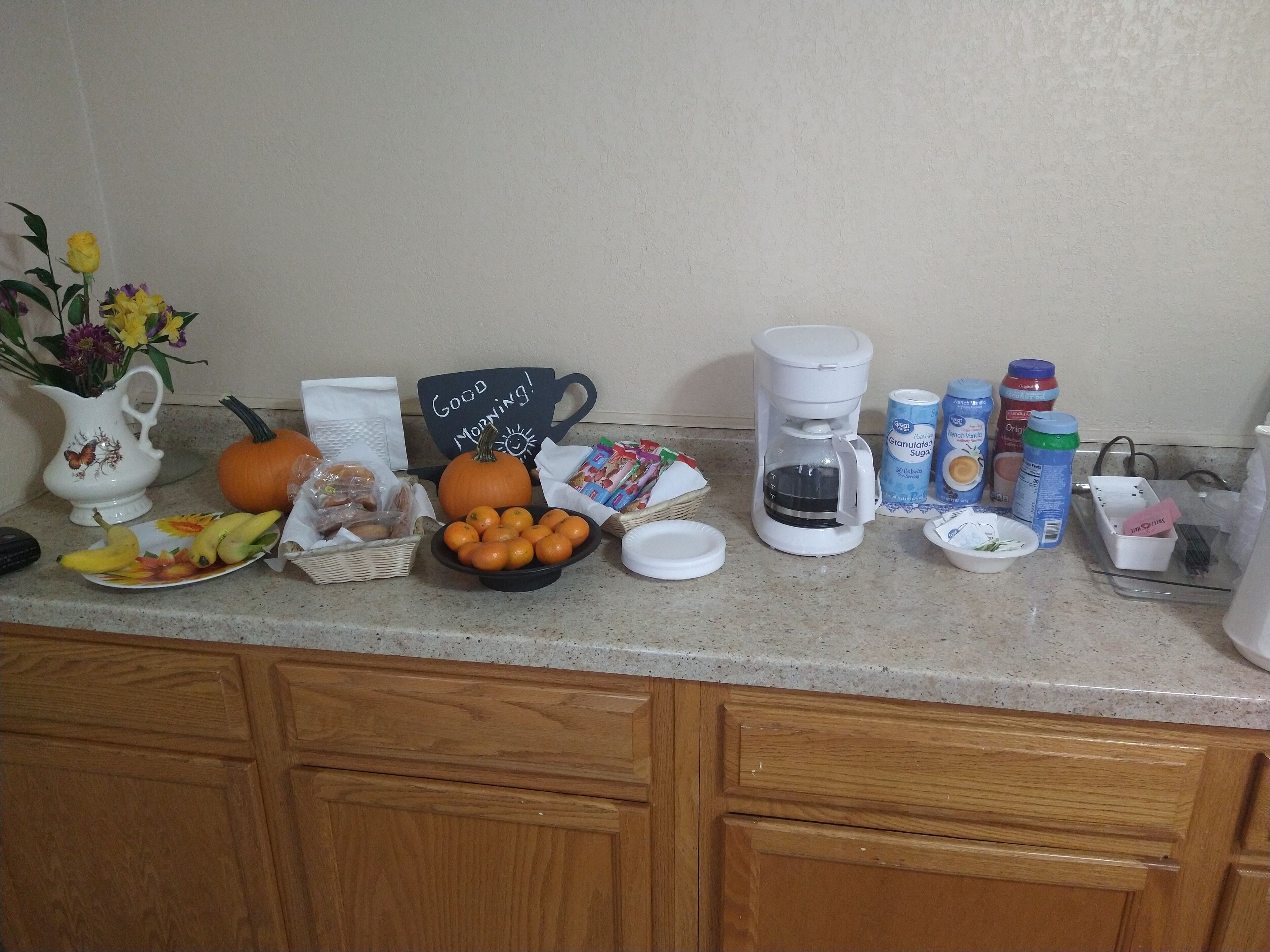 A kitchen counter with various breakfast items, including a coffee maker, orange juice, and a bowl of oranges.