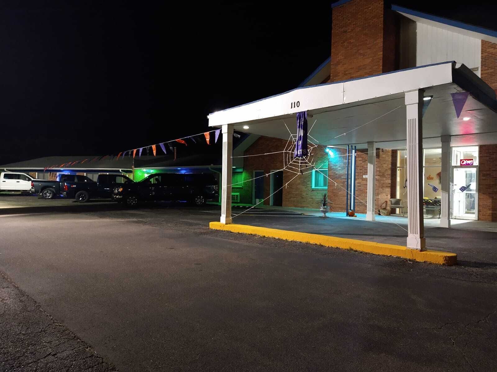 A covered outdoor area with a brick building, a white canopy, and a parking lot.