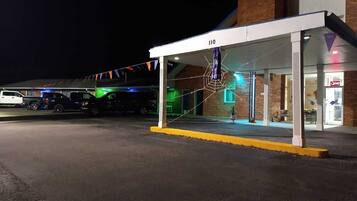 A covered outdoor area with a brick building, a white canopy, and a parking lot.