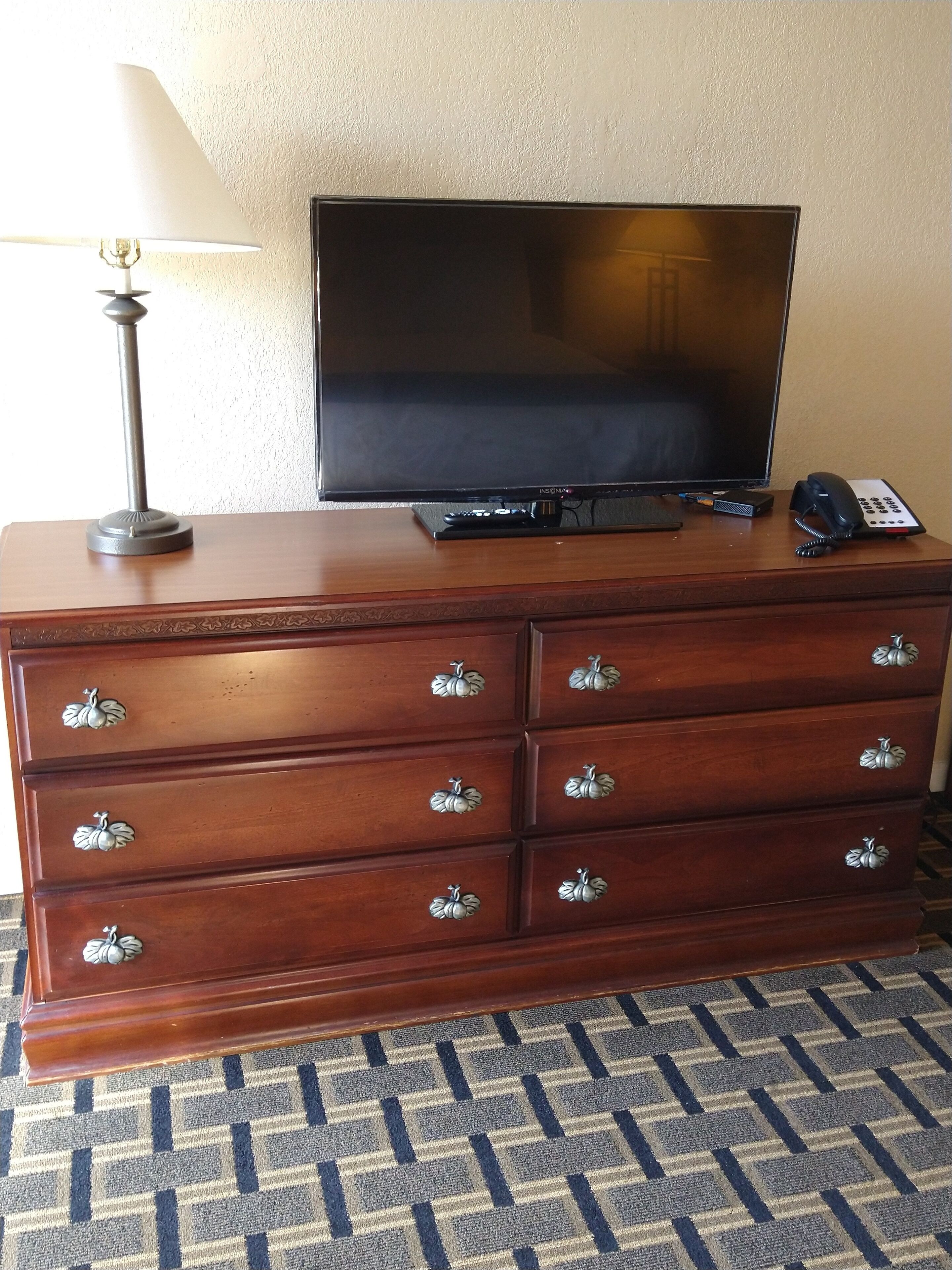 Une commode en bois, un téléviseur à écran plat, une lampe et un téléphone.
