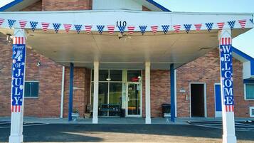 A building entrance with a covered area, a 'Welcome' sign, and a 'Happy 4th of July' banner.
