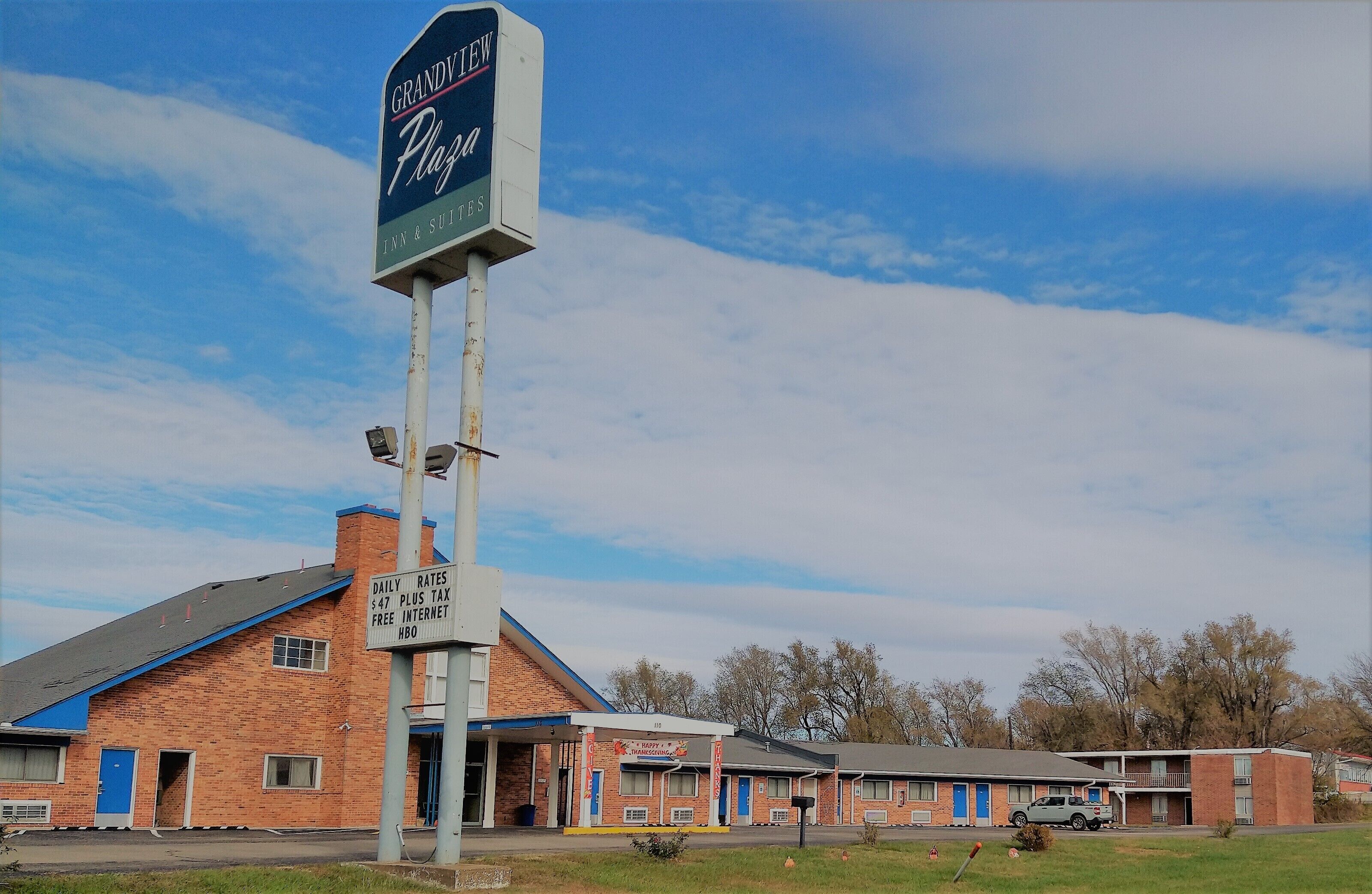 A motel with a sign for Grandview Plaza, featuring a brick building with blue accents, a parking lot, and a clear sky.