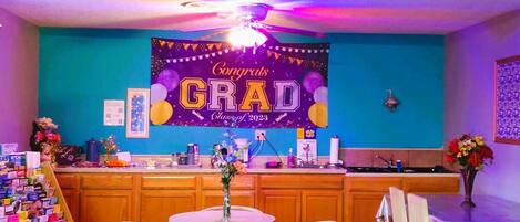 A room with a graduation banner, a small round table, chairs, a bar area, and a welcome sign.