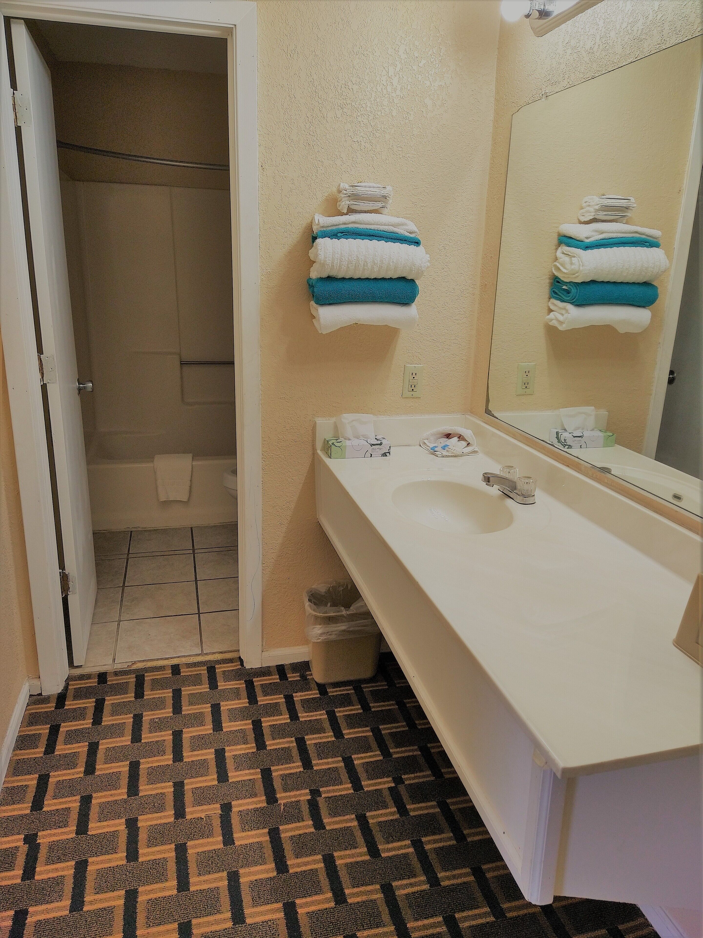 Une salle de bain avec un lavabo blanc, un miroir et des serviettes empilées sur le mur.