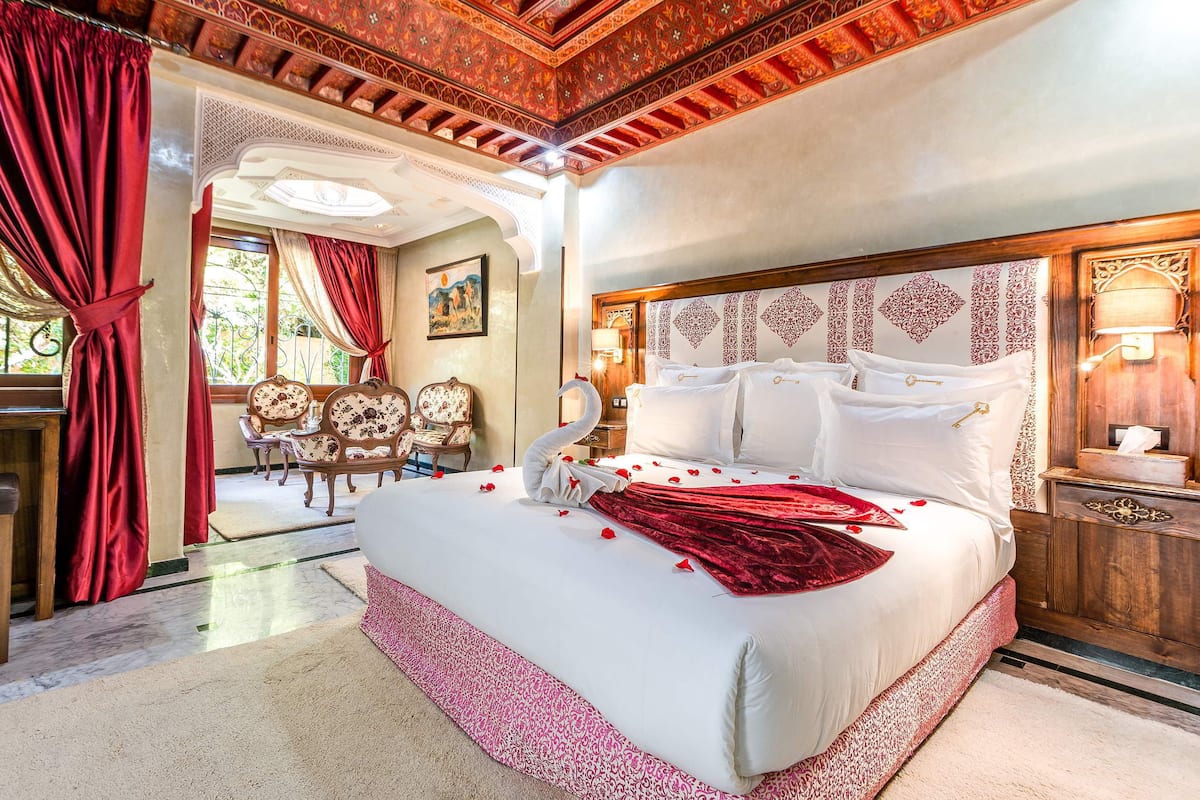 A spacious bedroom with a large bed, ornate headboard, and a chandelier.
