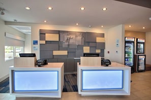 A hotel reception area with two reception desks, a Holiday Inn Express sign, a no smoking sign, and a beverage refrigerator.