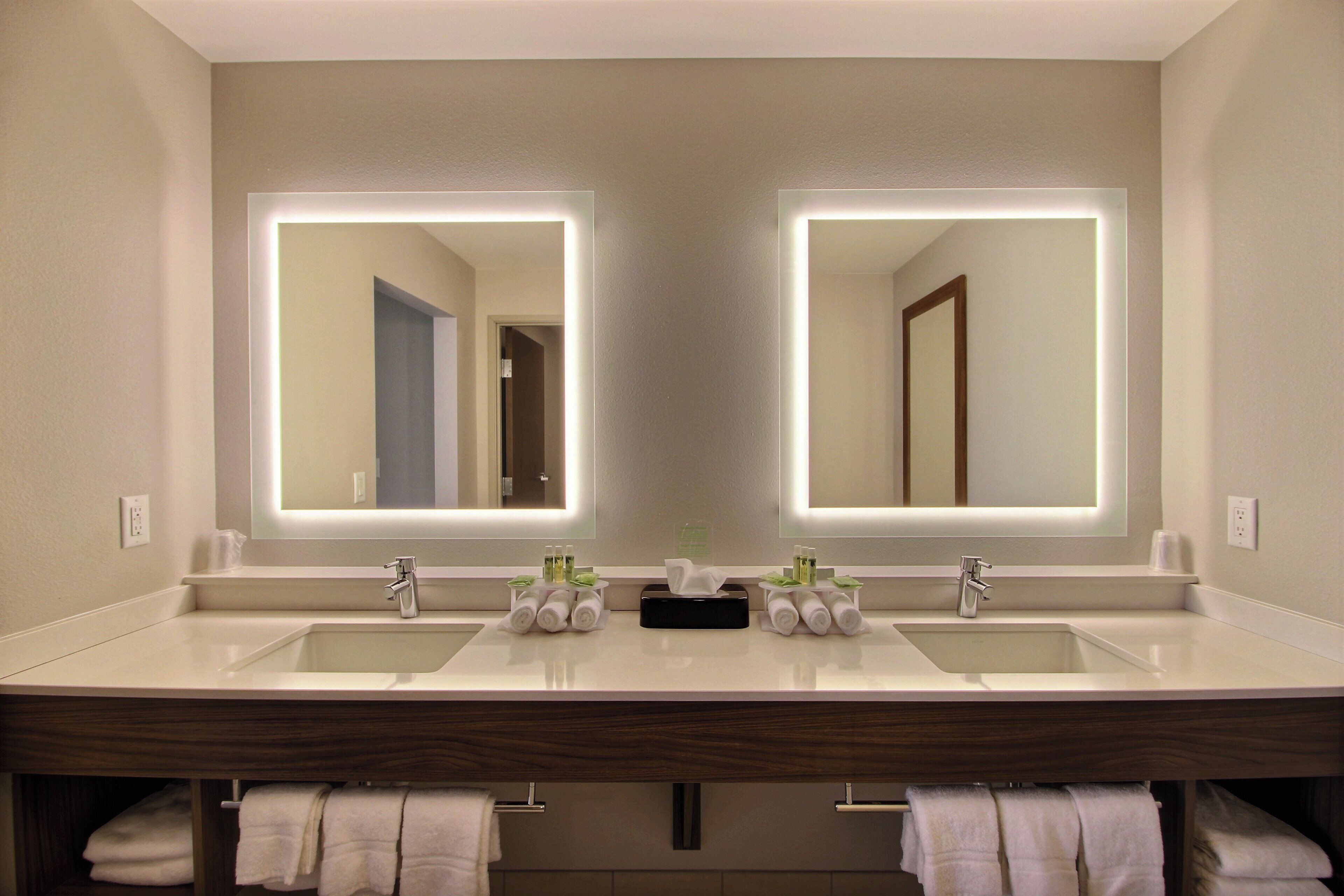 A hotel bathroom with two sinks, a mirror, and a towel rack.