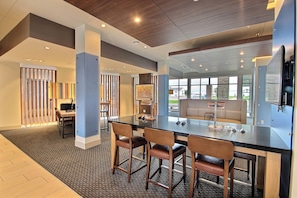 A modern interior with a long communal table, bar stools, and a seating area with a view.