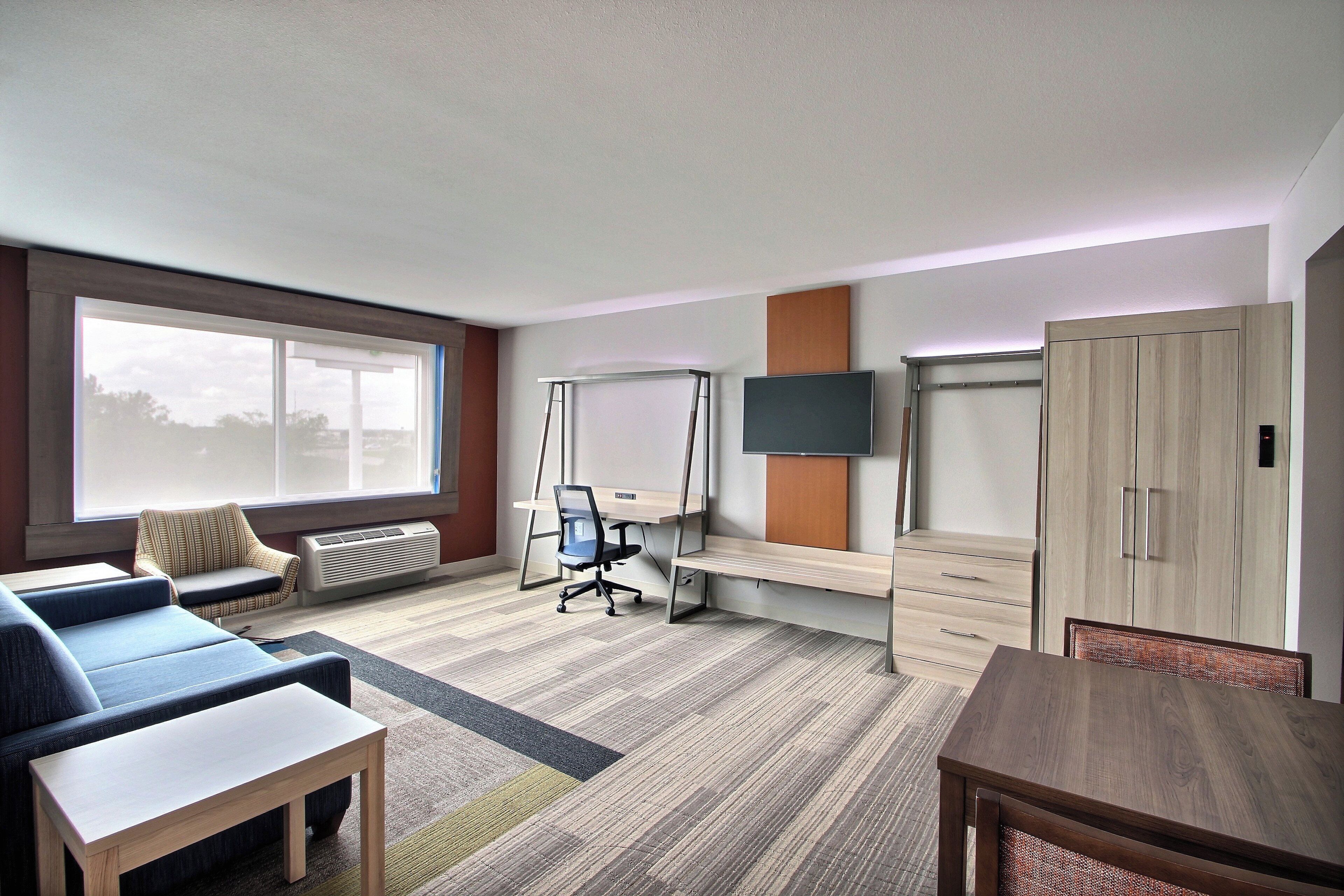 A hotel room with a sofa, a desk, a TV, a wardrobe, and a large window.