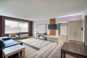 A hotel room with a sofa, a desk, a TV, a wardrobe, and a large window. - Holiday Inn Express & Suites Fond Du Lac by IHG (Fond du Lac)