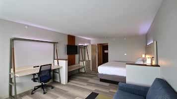 Habitación de hotel con cama, escritorio con silla, sofá, televisión y baño visible a través de una puerta abierta.