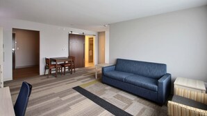 A modern living room with a blue sofa, a dining table with chairs, and a small side table. - Holiday Inn Express & Suites Fond Du Lac by IHG (Fond du Lac)