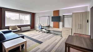 Une chambre d’hôtel moderne équipée d’un canapé, d’un bureau avec une chaise, d’un téléviseur fixé au mur et d’une armoire.