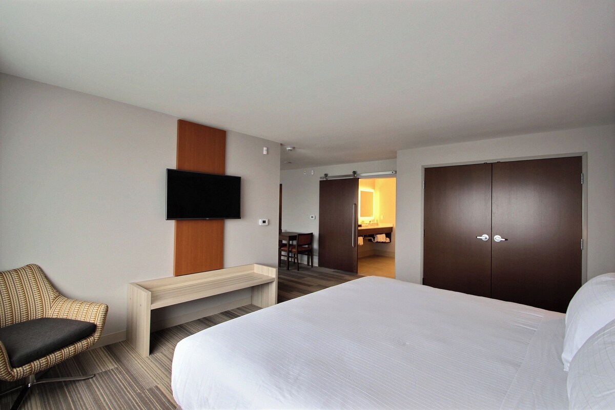 Hotelkamer met een bed, een aan de muur bevestigde televisie, een zithoek met een stoel en een garderobe.