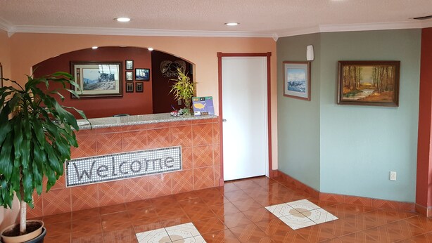 A reception area with a 'Welcome' sign, a reception desk, framed pictures on the walls, and a potted plant. - Budget Inn (Eastland)