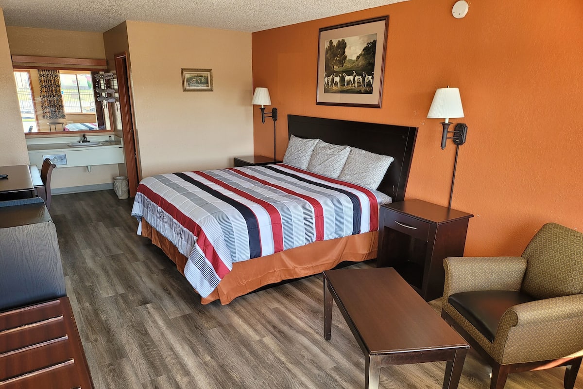 A hotel room with a bed, a desk, a chair, and a small table.