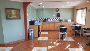 A kitchen with wooden cabinets, a tiled floor, and a dining area with chairs. - Budget Inn (Eastland)