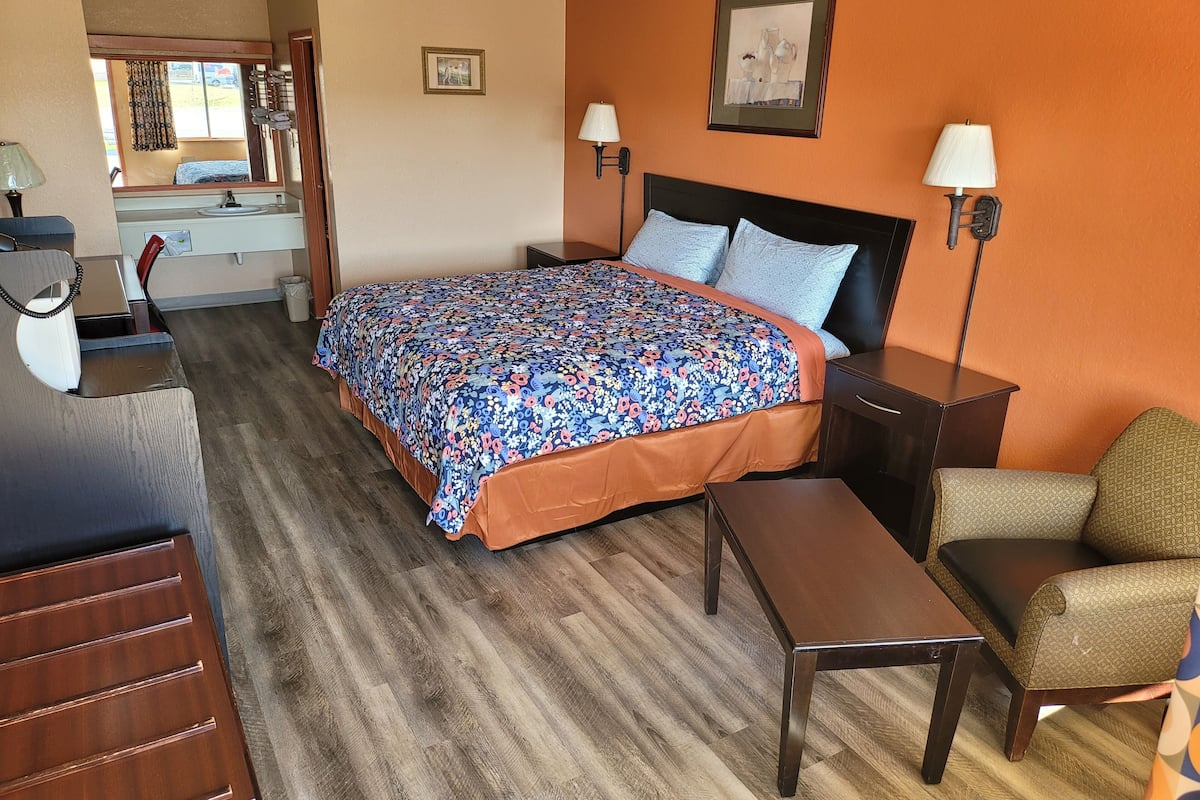 A hotel room with a bed, bedside tables, a desk, a chair, and a mirror.