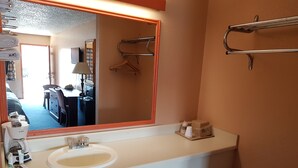 A hotel bathroom with a large mirror, a sink, a towel rack, and a small trash bin. - Budget Inn (Eastland)