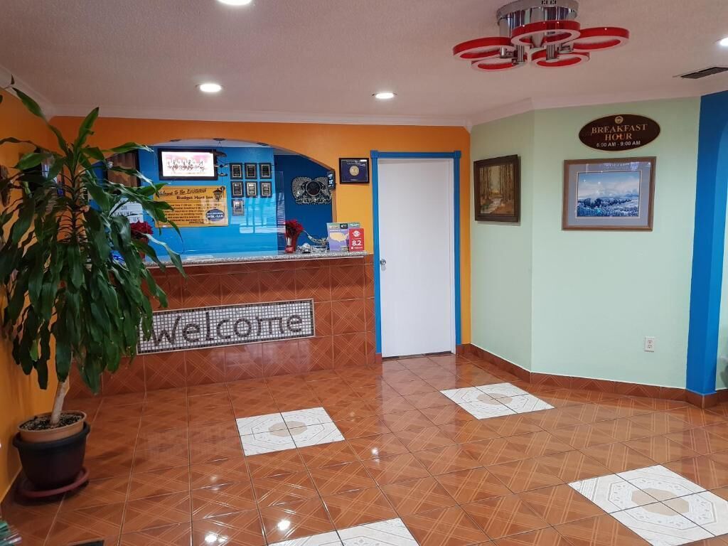Ein Empfangsbereich mit einem 'Welcome'-Schild, einem Empfangstresen, einer Tür und einer Wand mit einem 'Breakfast Hour'-Schild.