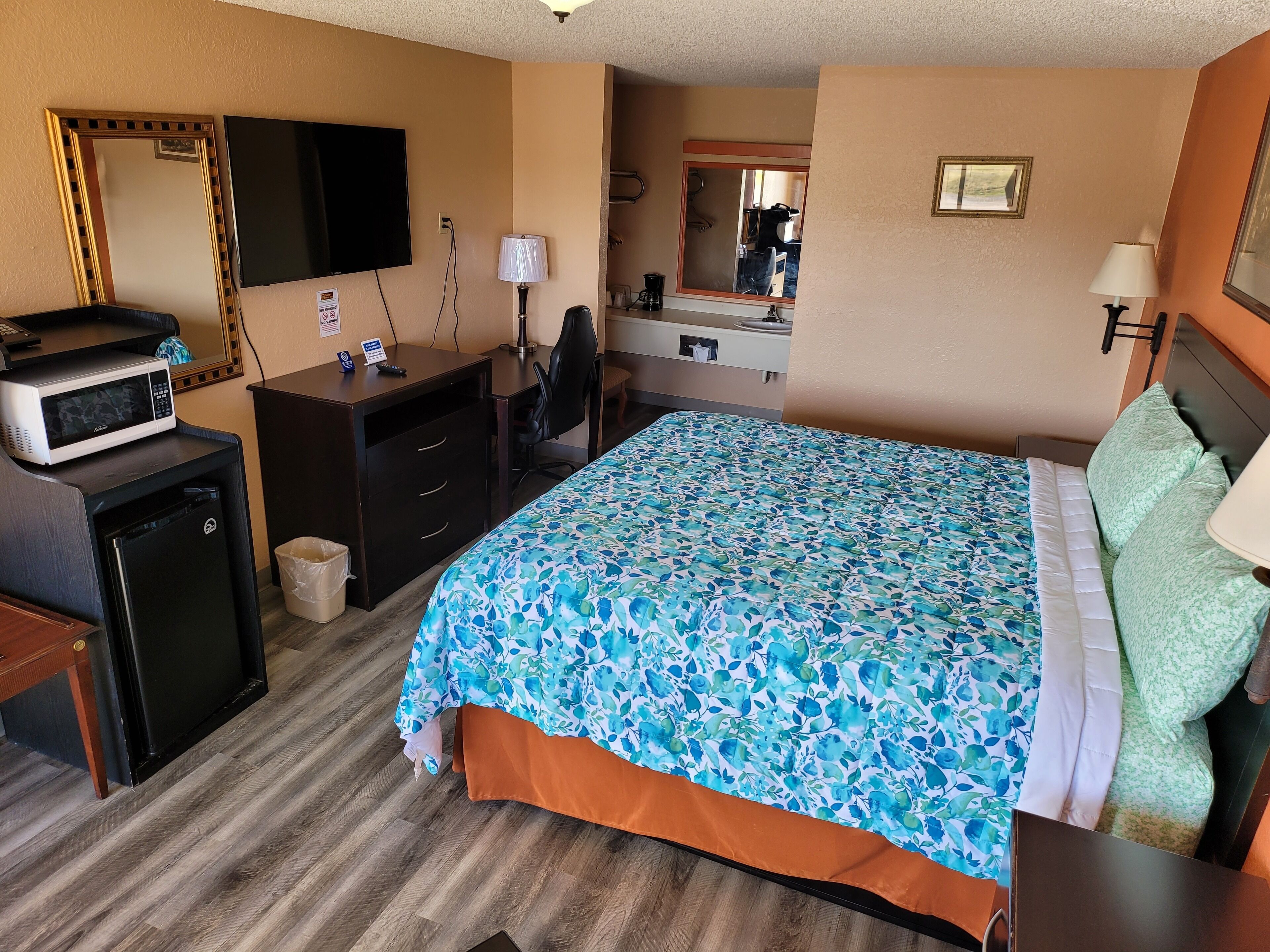 A hotel room with a bed, desk, microwave, and a small refrigerator.