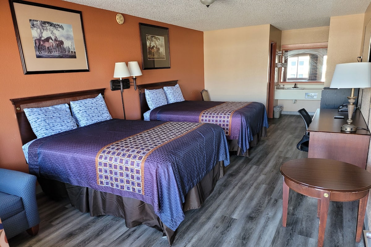 A hotel room with two beds, a desk, a chair, and a small table.