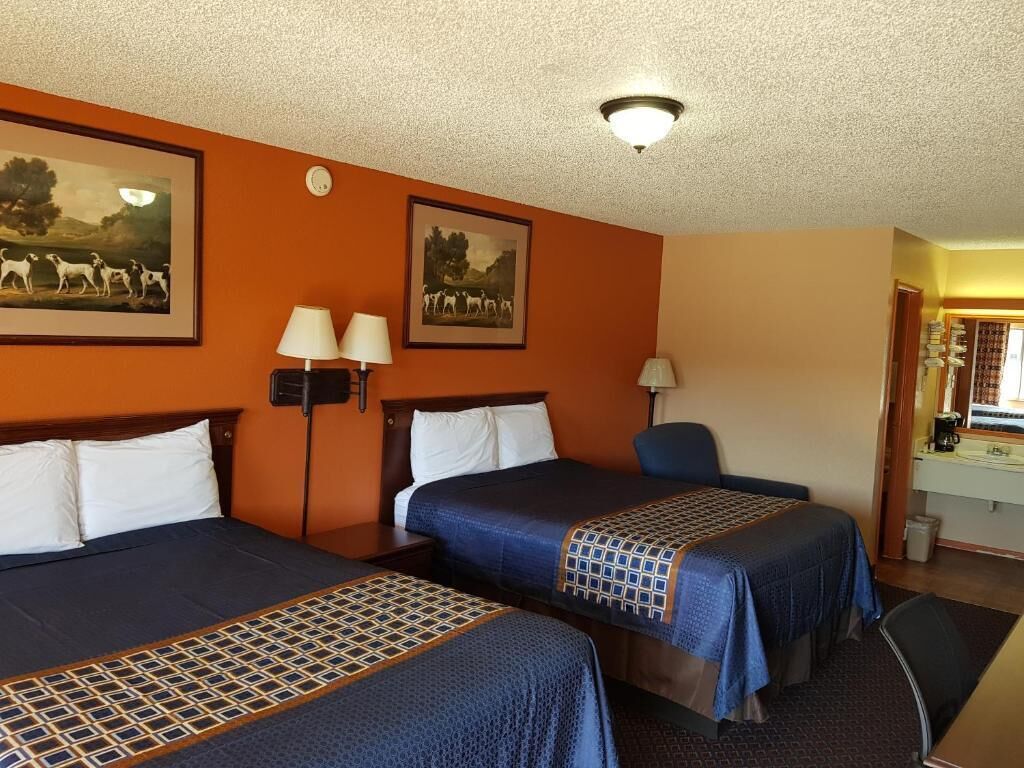 Ett hotellrum med två sängar, ett skrivbord, en stol och ett badrum som syns genom en öppen dörr.