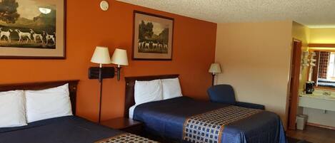 A hotel room with two beds, a desk, a chair, and a bathroom visible through an open door.