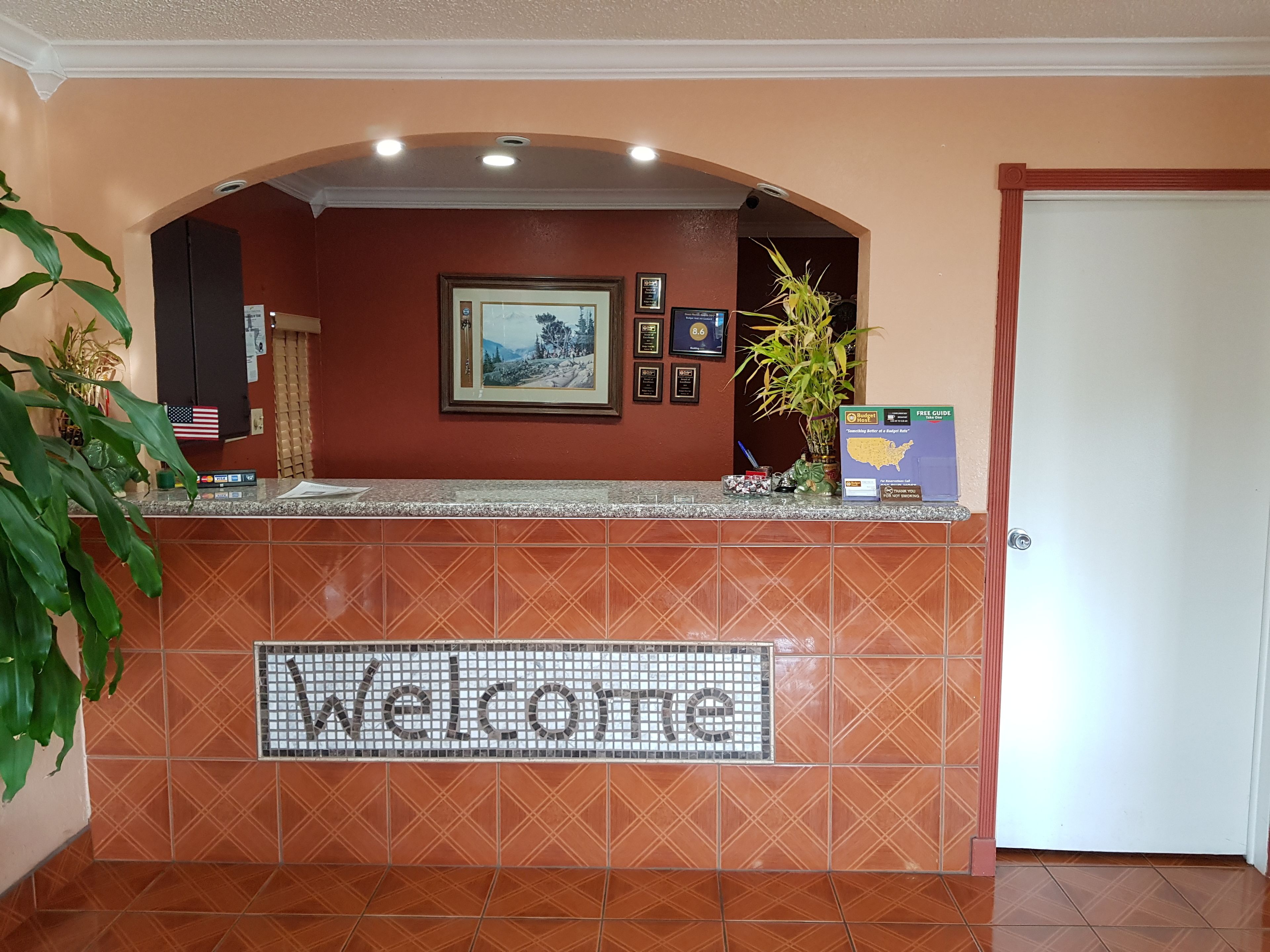 Una zona de recepción con un cartel de 'Welcome', un cuadro enmarcado y un cartel de 'Budget Inn'.