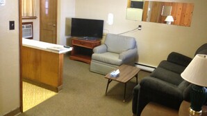 A compact living room with a television, a sofa, a chair, and a small table. - Jamestown Motel (Jamestown)