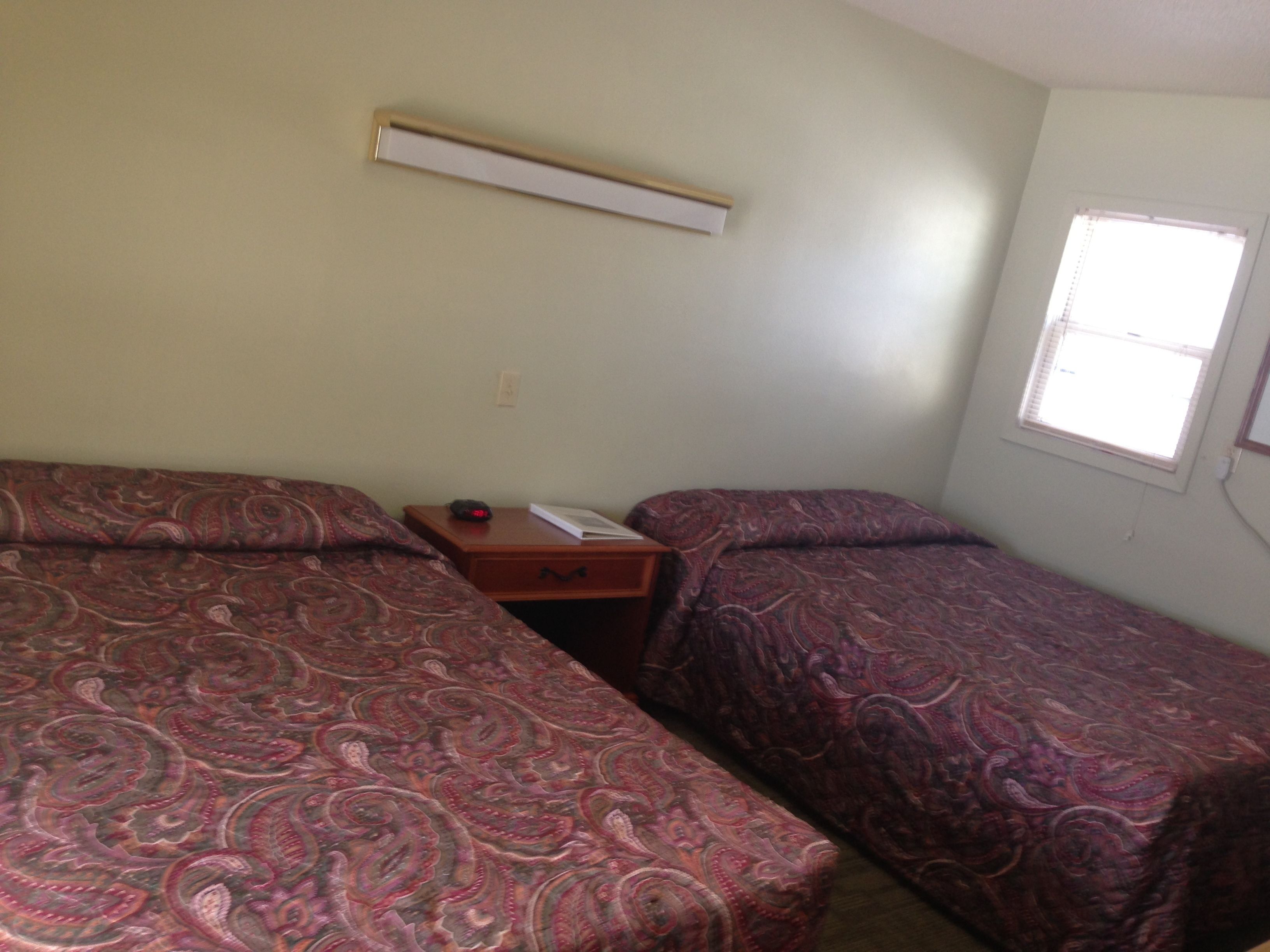 Een kamer met twee bedden, een nachtkastje, een wandairconditioner en een raam.