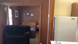 A compact living space with a sofa, a bed, a small table, and a refrigerator. - Jamestown Motel (Jamestown)
