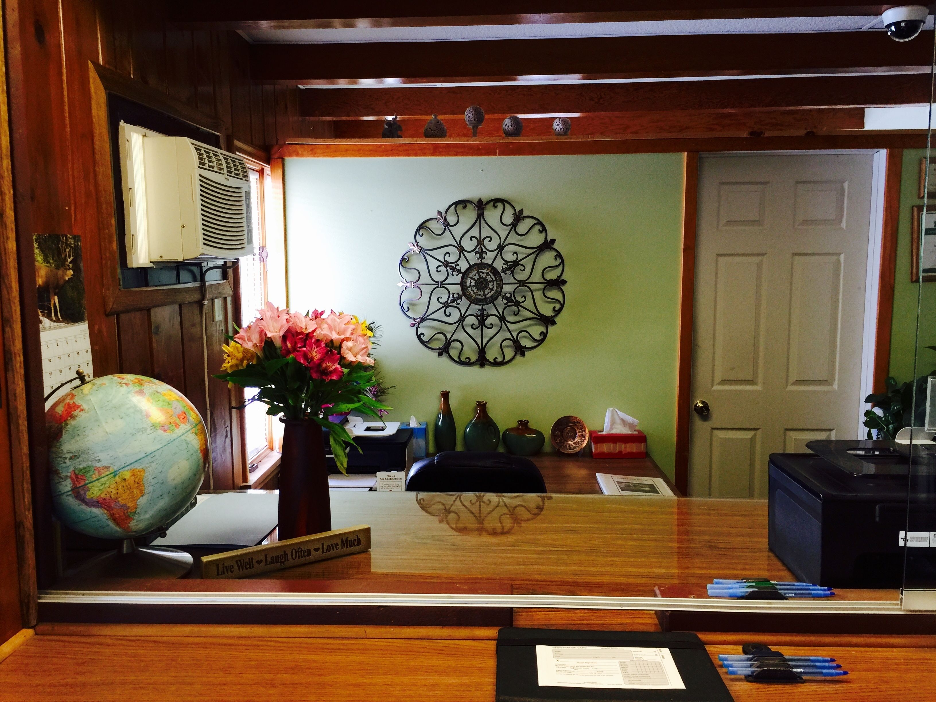 Un mostrador de recepción con un globo terráqueo, un jarrón de flores, un adorno de pared y paneles de madera.