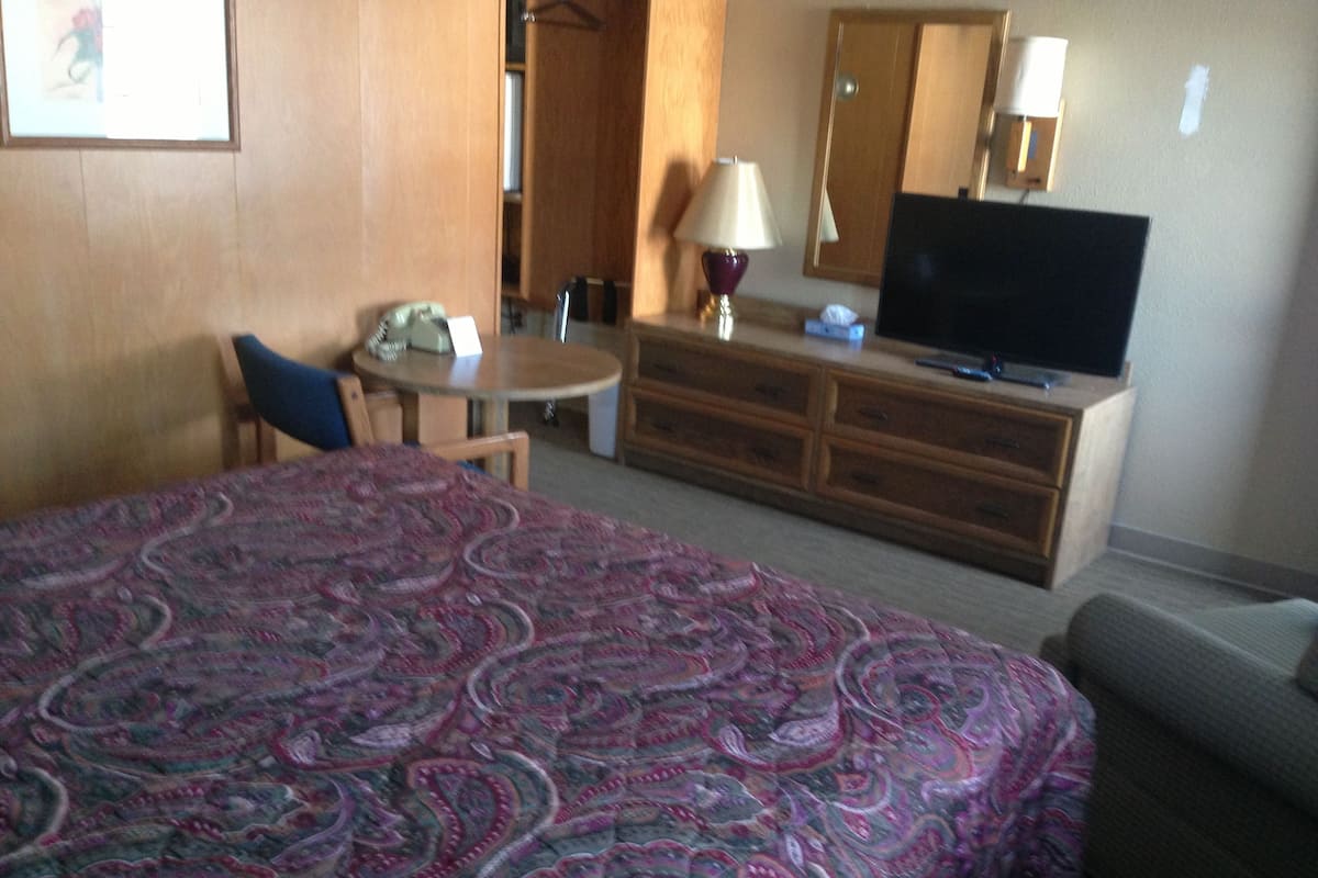 A hotel room with a bed, a desk, a chair, a dresser, a television, and a lamp.