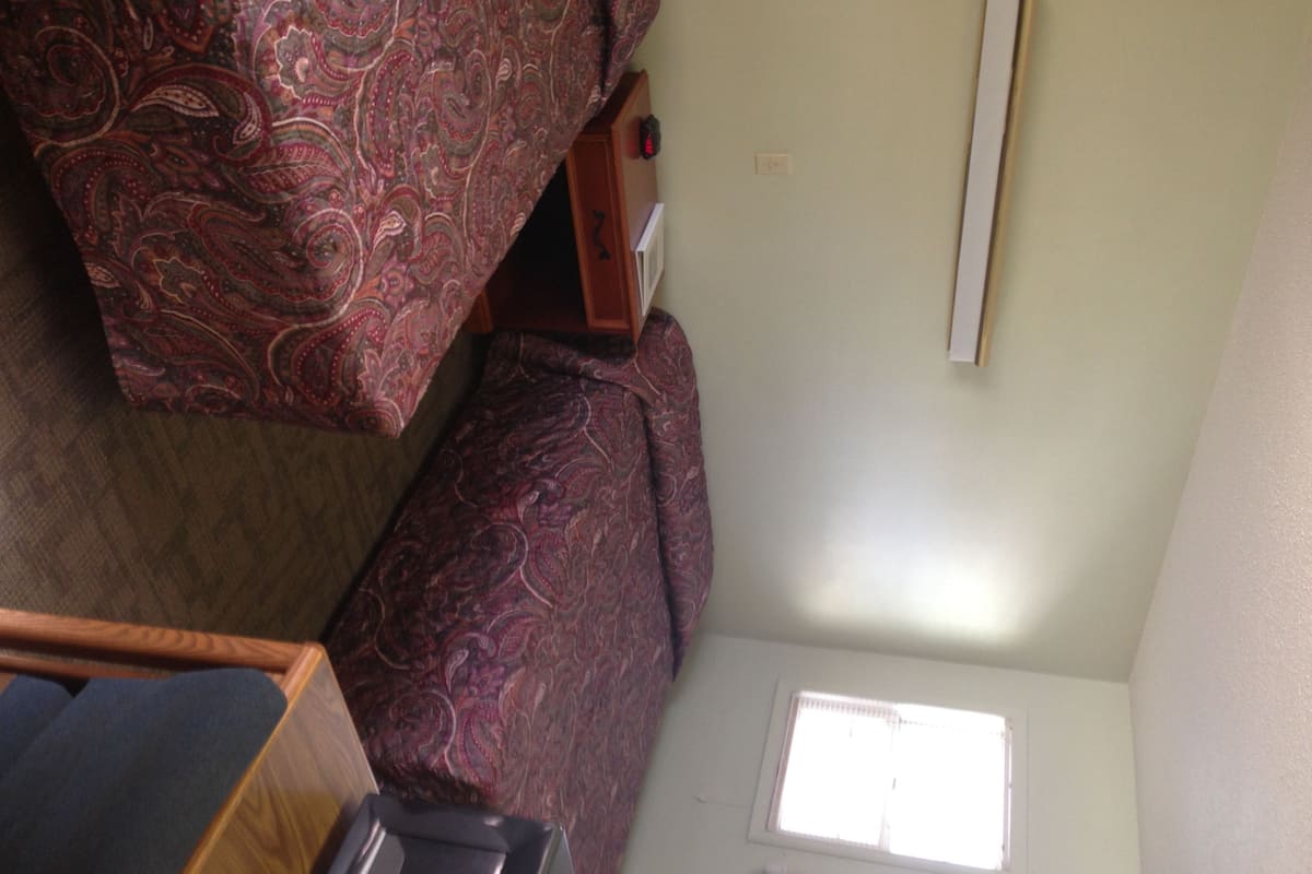 A compact RV interior with a bed, a small table, and a window.