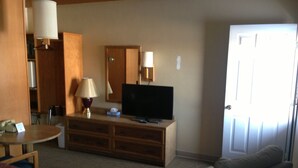 A hotel room with a bed, a sofa, a television, a desk with a lamp, and a door. - Jamestown Motel (Jamestown)