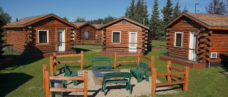 A row of log cabins with outdoor seating areas and a clear sky.