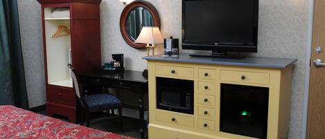 A hotel room with a bed, a wardrobe, a desk with a chair, a television, a microwave, and a lamp.