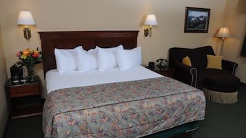 Habitación de hotel con una cama grande, dos lámparas de noche, una silla, una mesita y un cuadro en la pared.