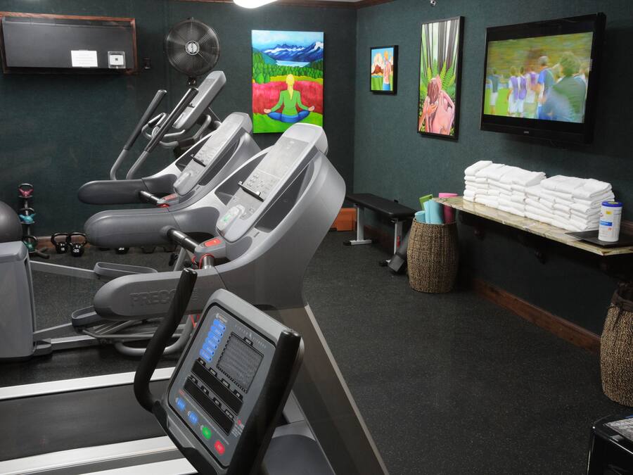 Ett gym med löpband, en motionscykel och en tv som är monterad på väggen.