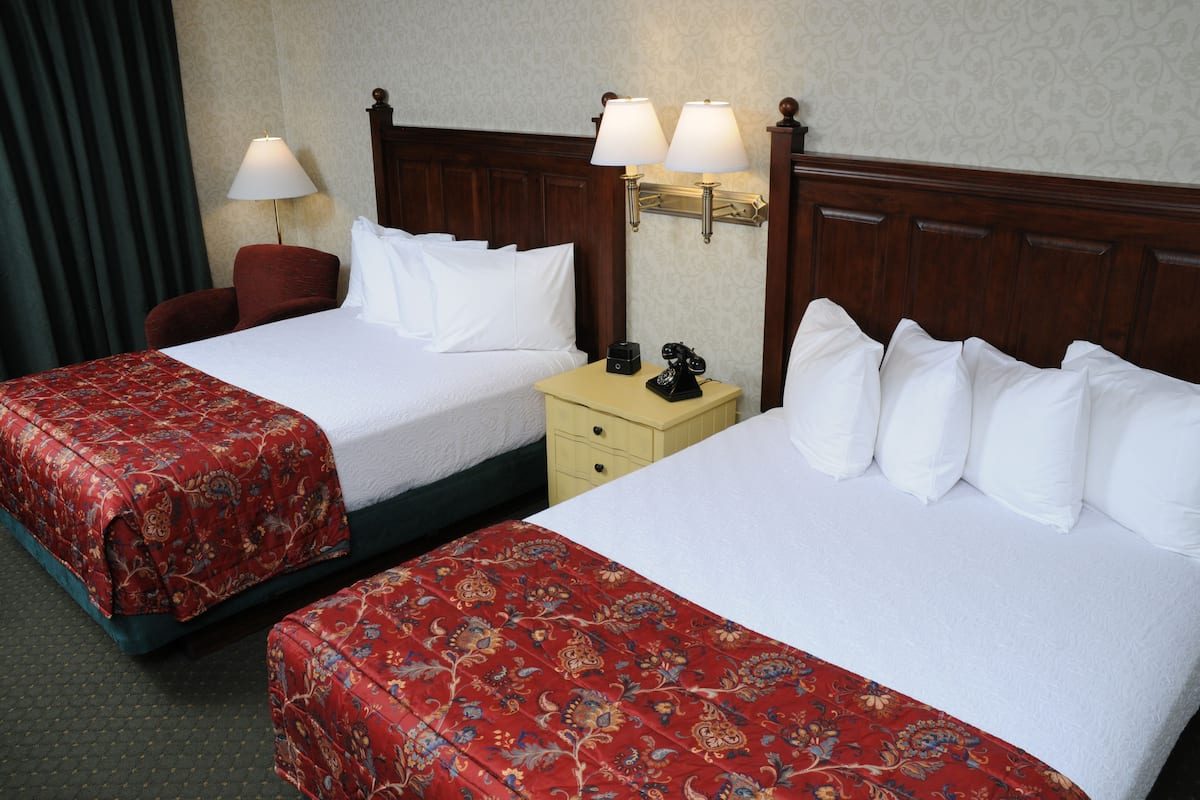 Two double beds with red and white bedding, wooden headboards, bedside lamps, and a small bedside table with a telephone and a decorative item.