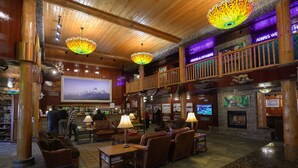 A lobby with wooden beams, a fireplace, and a large TV screen. - Pike's Waterfront Lodge (Fairbanks)