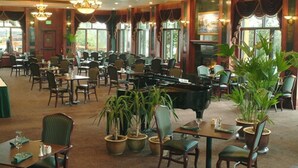 A spacious restaurant with multiple tables and chairs, potted plants, and a grand piano. - Pike's Waterfront Lodge (Fairbanks)