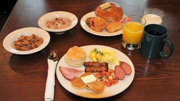 Ein reichhaltiges Frühstücksbuffet auf einem Holztisch mit Pfannkuchen, Würstchen, Eiern und Toast.