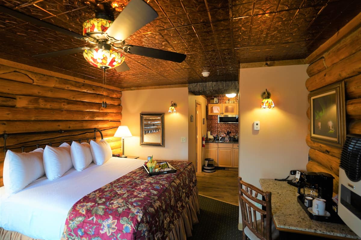 A wooden cabin room with a bed, a dining table, and a kitchen area.
