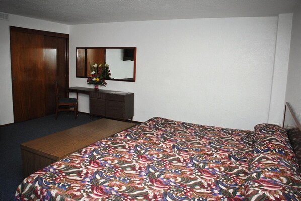 A bedroom with a bed, a desk, a chair, a dresser, and a mirror.