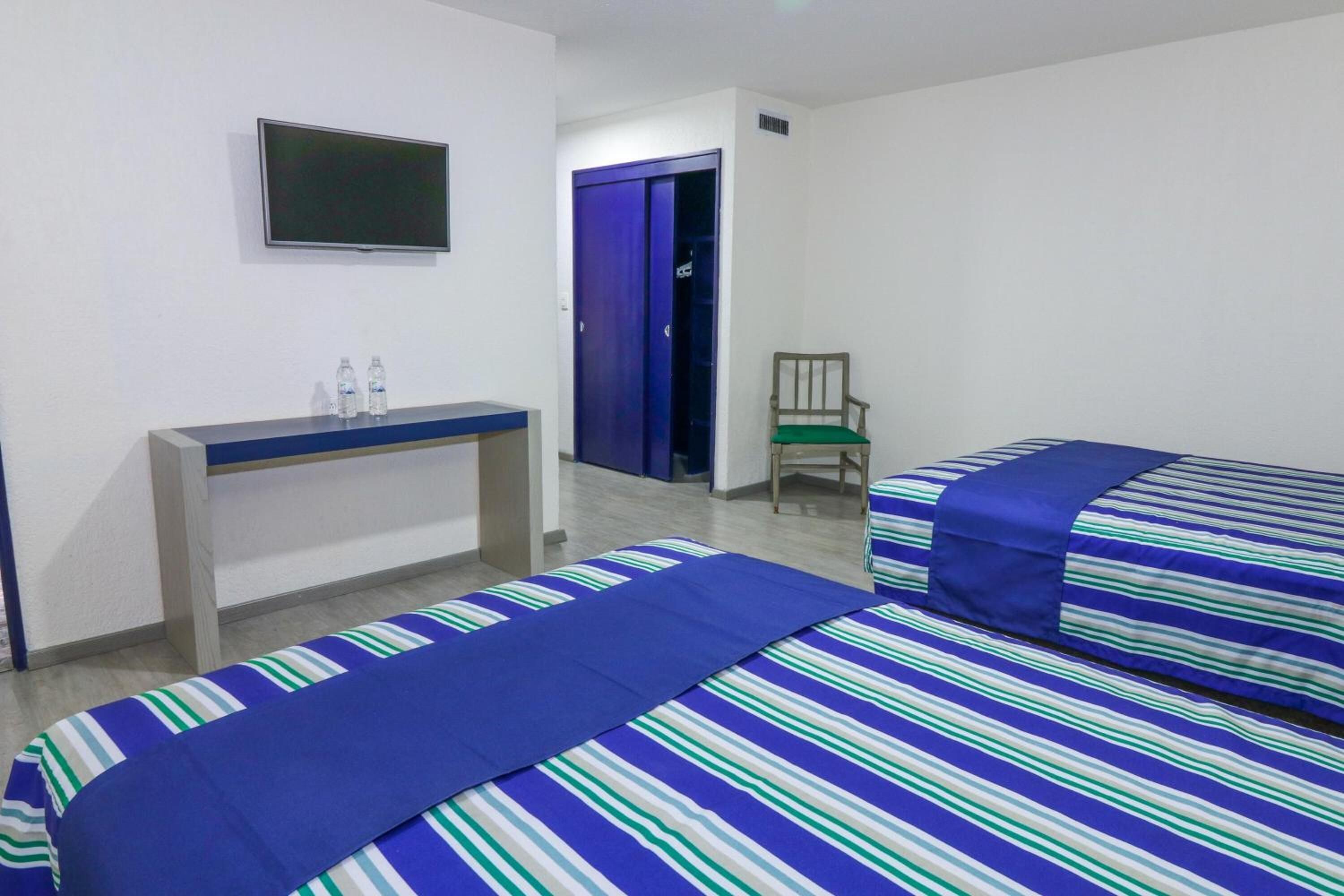 Camera d'albergo con due letti, televisione, scrivania e bottiglie d'acqua, e una sedia.