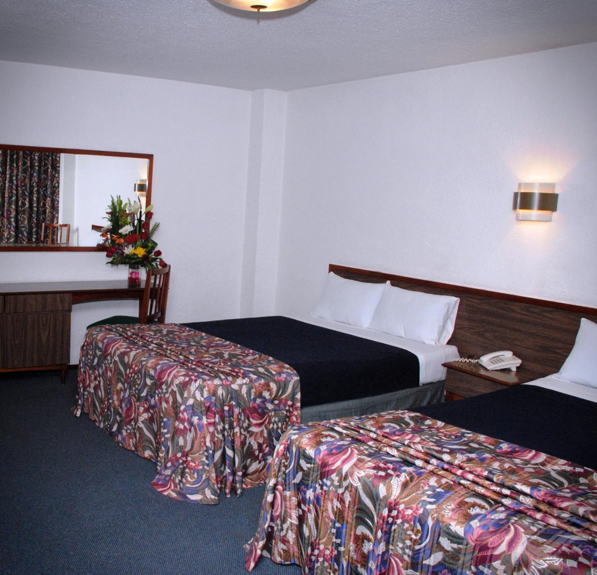 A hotel room with two beds, a desk, a chair, a mirror, and a nightstand with a phone.