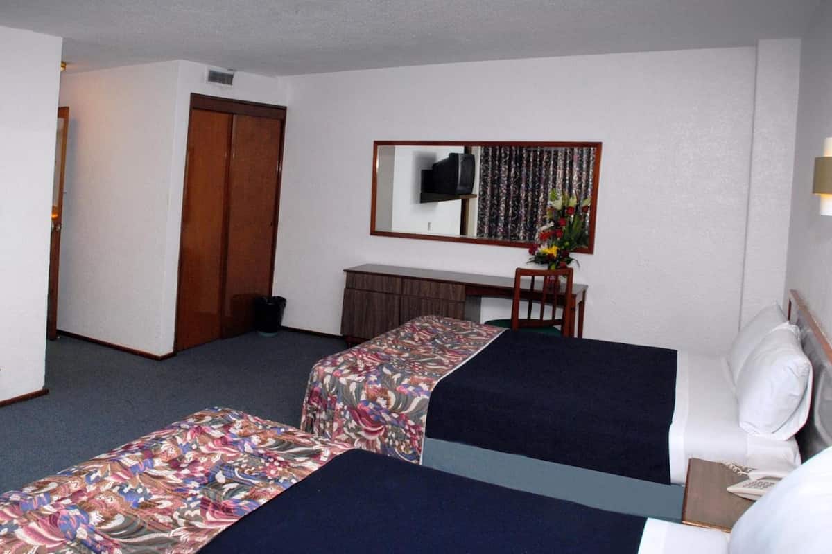 A hotel room with two beds, a desk, a chair, a TV, a mirror, and a small trash bin.